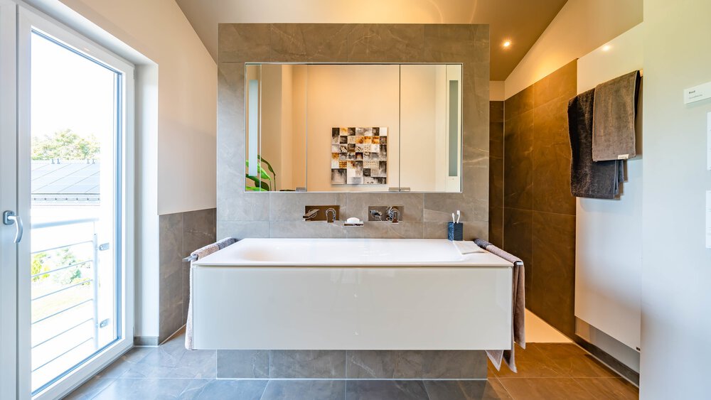Modernes Badezimmer mit großem Spiegel, hängendem Waschbecken, Handtüchern, begehbarer Dusche und einem raumhohen Fenster, das für Tageslicht sorgt.