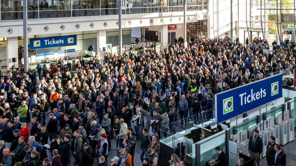 Large crowd of visitors in an exhibition entrance hall in front of the ticket counters.