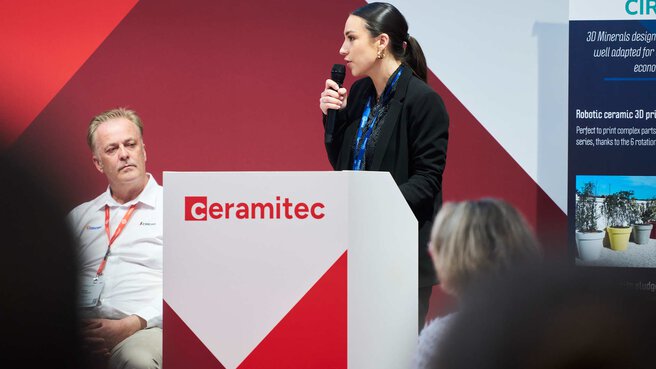 Speaker presenting on the ceramitec stage at a podium in front of an audience.