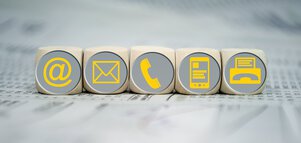 Fünf Würfel nebeneinander mit gelben Symbolen auf der Vorderseite: E-Mail, Brief, Telefon, Handy und Fax.