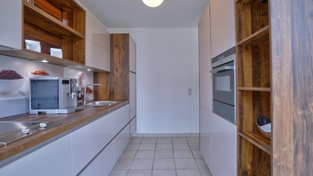 Moderne Kombüsenküche mit Holzregalen, eleganten Schränken, eingebautem Ofen, Kaffeemaschine und Fliesenboden.