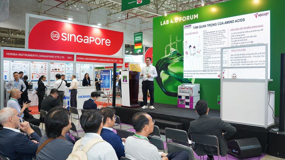 Man gives a presentation on amino acids on stage at the LAB 4.0 Forum; the audience is seated, the Singapore stand can be seen behind him.