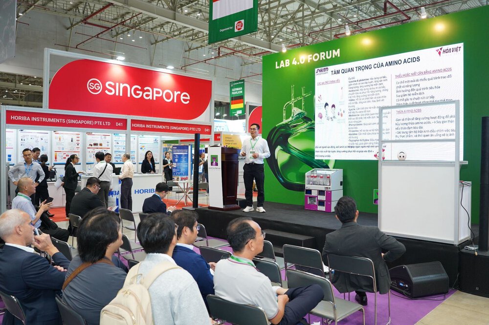 Man gives a presentation on amino acids on stage at the LAB 4.0 Forum; the audience is seated, the Singapore stand can be seen behind him.