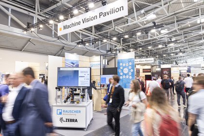 Besucher, die über die Ausstellung Machine Vision Pavilion laufen. Im Hintergrund sind Mesestände zu sehen