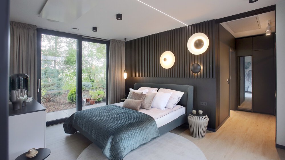 Modernes Schlafzimmer mit Doppelbett, großem Fenster, runden Lichtern an der Wand und einer grünen Überwurfdecke.