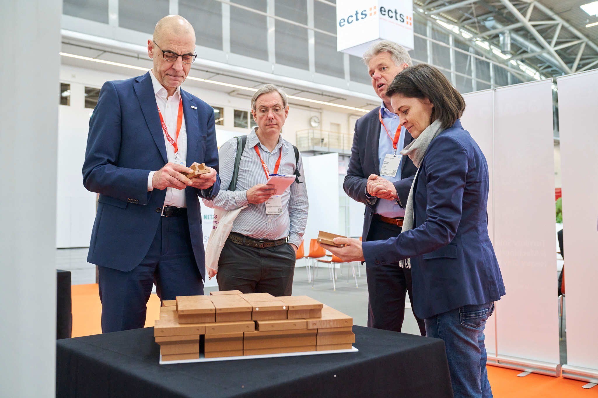 Four trade fair visitors examine ceramic samples together at a table.