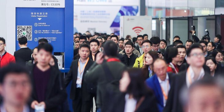 Numerous visitors to Messe München Shanghai move through the entrance area, past a blue stele bearing the words “Visitor Registration”.