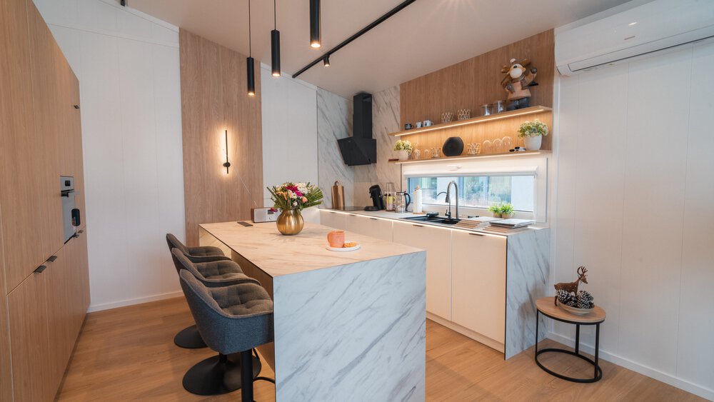 Eine moderne Küche mit Holzwänden, einem Marmortesen und einer weißen Küchenzeile mit schwarzer Abzugshaube und Regalbrettern.