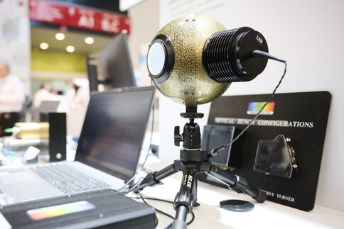 An optoelectronic measuring device with a spherical, gold-colored housing and LED light source, mounted on a tripod and connected to a laptop.