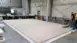 Two men unroll a large beige tarpaulin on the floor of a spacious industrial hall