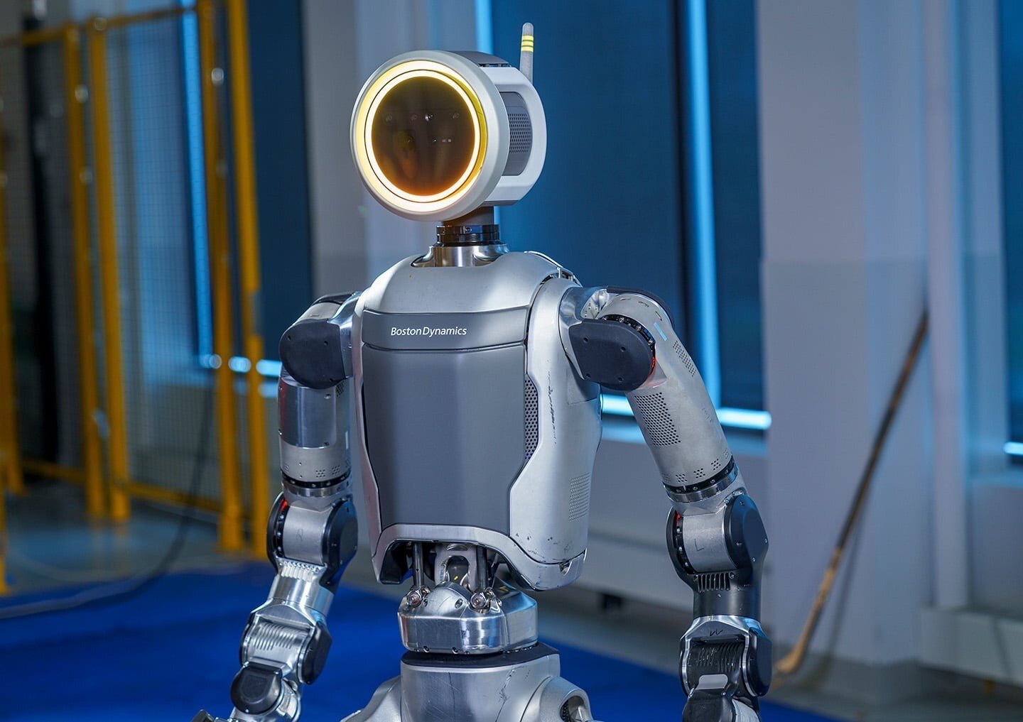 Humanoid robot with a round head and electronics, standing in a test environment.