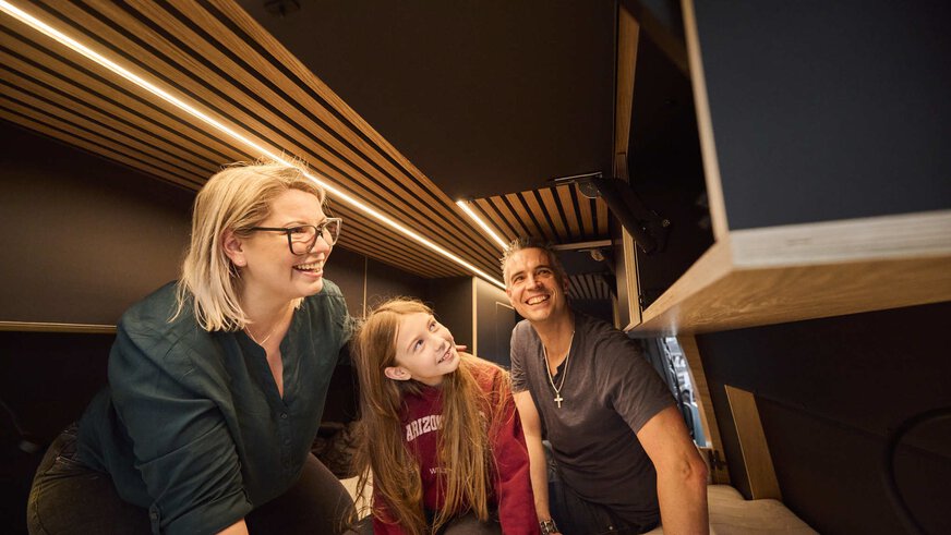 Parents with children take an enthusiastic look at the inside of a converted camper van.