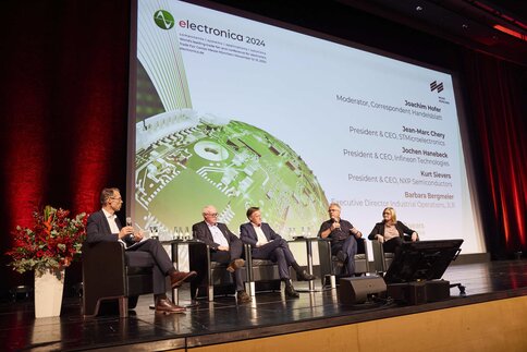 Podiumsdiskussion mit fünf Sprechern auf der Bühne. Auf dem großen Bühnendisplay stehen Informationen zu den Sprechern neben dem Keyvisual der electronica.