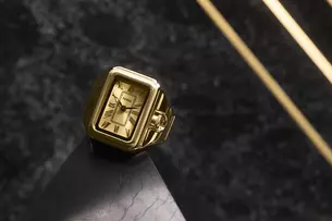 Goldene Uhr mit römischen Ziffern auf schwarzer Marmoroberfläche und diagonalen goldenen Linien im Hintergrund.