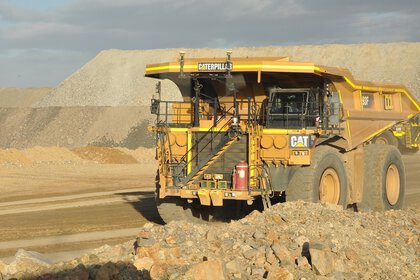 Ein großer gelber CAT-Muldenkipper in einem Kieswerk, mit Schotterhaufen im Hintergrund bei Sonnenschein.