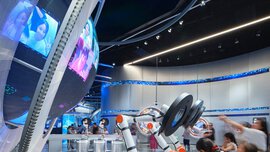 A large silver-framed globe with several video stations in front of it, where visitors are filmed and projected onto the globe.