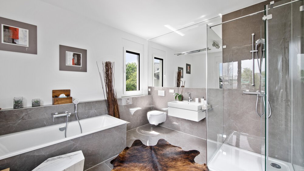 Modernes Badezimmer mit Glasdusche, Badewanne, Toilette und Waschbecken. Zur Einrichtung gehören Kunstwerke, hohe Vasen und ein Teppich auf dem Boden.