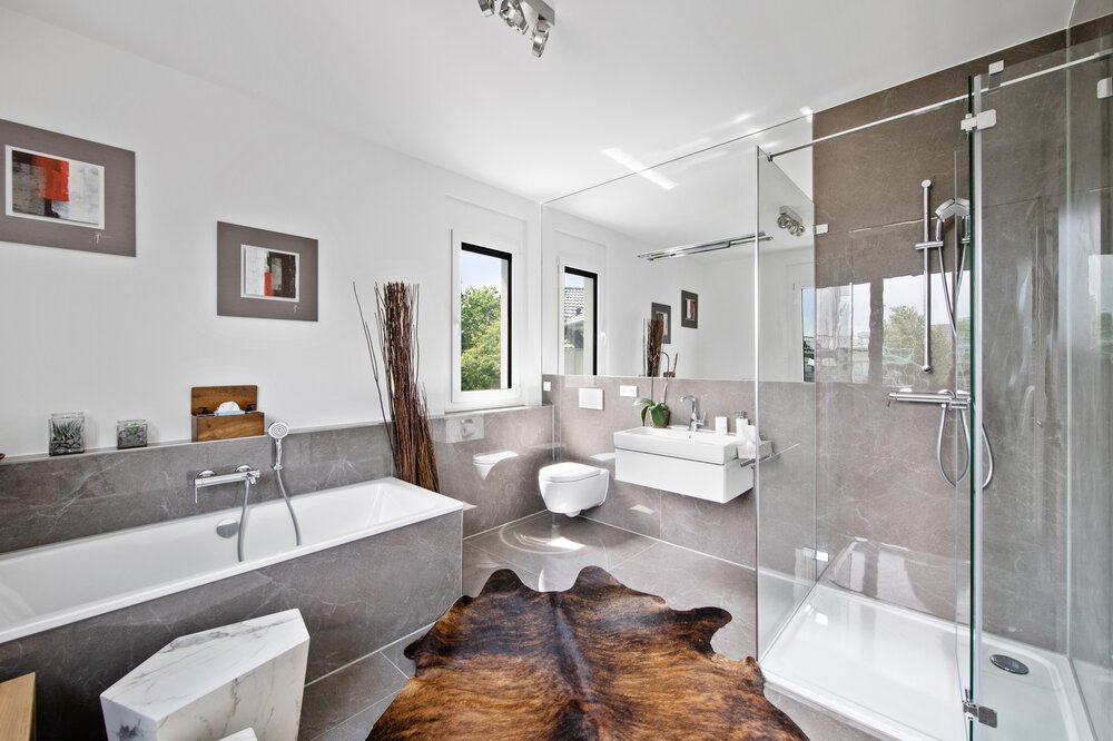 Modernes Badezimmer mit Glasdusche, Badewanne, Toilette und Waschbecken. Zur Einrichtung gehören Kunstwerke, hohe Vasen und ein Teppich auf dem Boden.