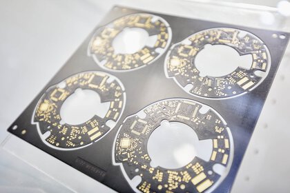 Nahaufnahme von vier identischen runden Leiterplatten, die noch in einer schwarzen Stanzform hängen.