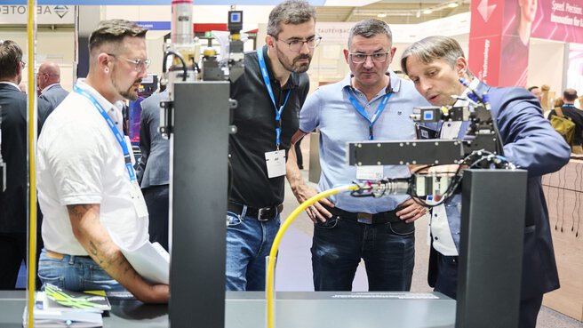 Vier Männer betrachten ein technisches Exponat auf der Laser World of Photonics 2025 in München.