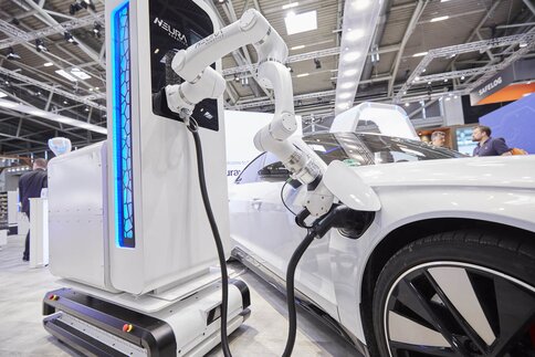 At an exhibition stand, a robotic arm connects a charging cable to a car.