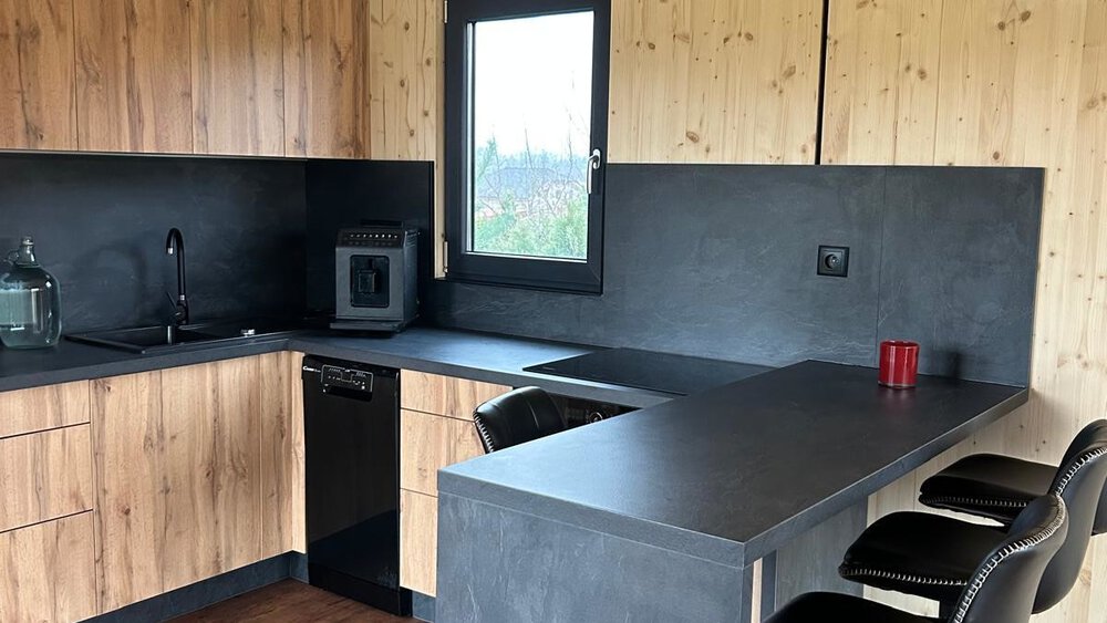 Moderne Küche mit schwarzen Arbeitsplatten, Holzschränken, schwarzen Barhockern und Holzboden.