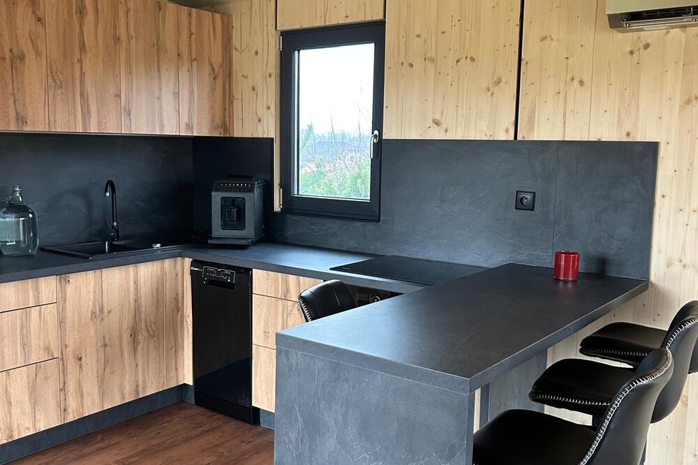 Moderne Küche mit schwarzen Arbeitsplatten, Holzschränken, schwarzen Barhockern und Holzboden.