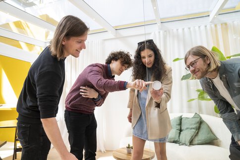 Drei Männer und eine Frau betrachten interessiert den Knauf eine Glastür an einem Messestand auf der BAU.