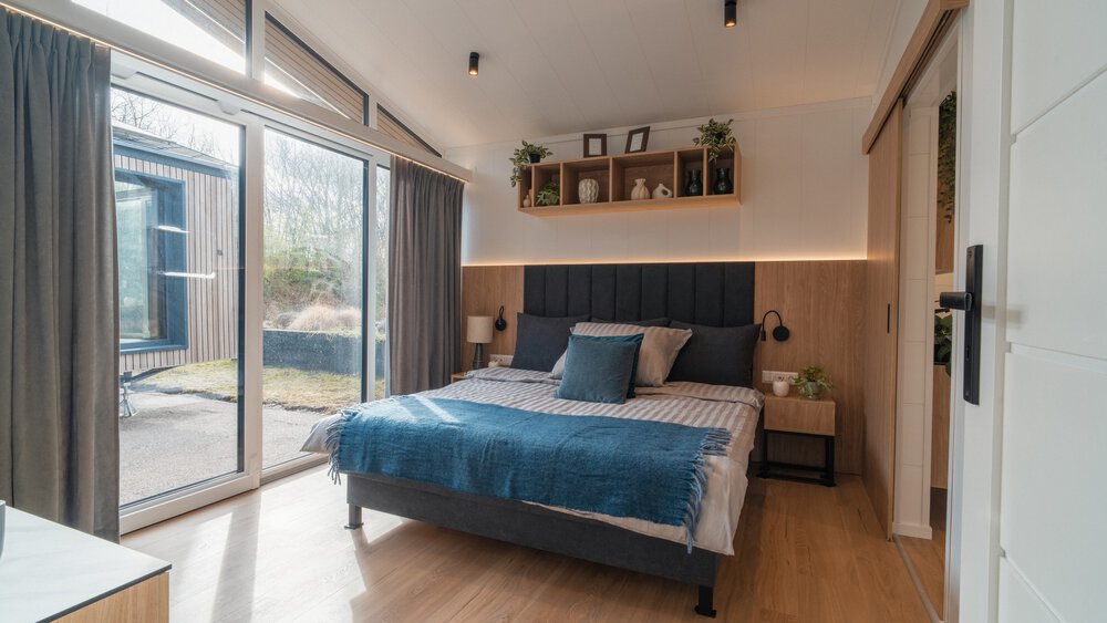 Ein großes Schlafzimmer mit schräger Decke, großer gläserner Schiebetür zu einer Terrasse und einem großen Doppelbett mit zwei Beistelltischen.