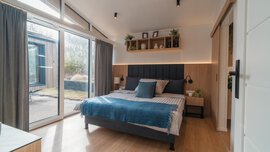 Ein großes Schlafzimmer mit schräger Decke, großer gläserner Schiebetür zu einer Terrasse und einem großen Doppelbett mit zwei Beistelltischen.