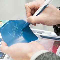 A hand writes with a pen on a flexible display made of blue plastic.