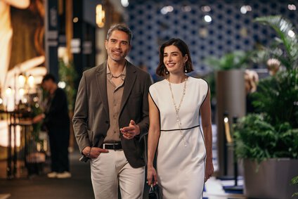 Ein Mann und eine Frau in festlicher Kleidung laufen lächelnd und interessiert durch eine Ausstellungshalle der INHORGENTA.