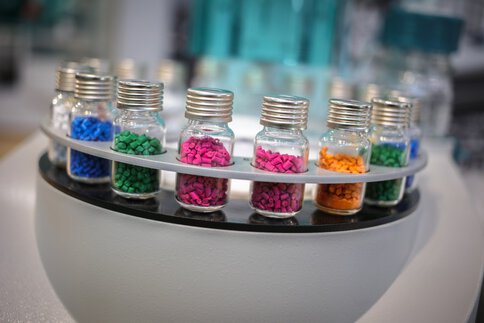 Nahaufnahme eines Analysegeräts: In runden Halterungen sind im Kreis mehrere Fläschchen mit Aluminium-Septumverschluss (Vials) mit bunten Körnern gefüllt angeordnet.