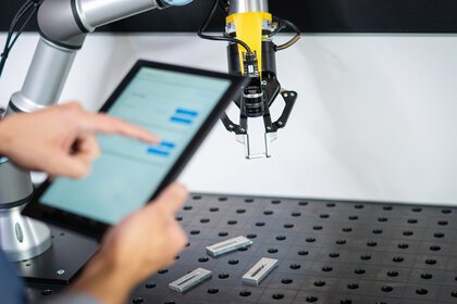 Person controlling a robot arm with a gripper tool using a tablet.