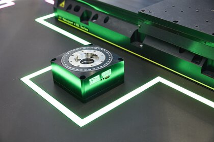 A square, metallic base with a round dial bearing compass numbers is framed by a glowing green line on a dark surface.