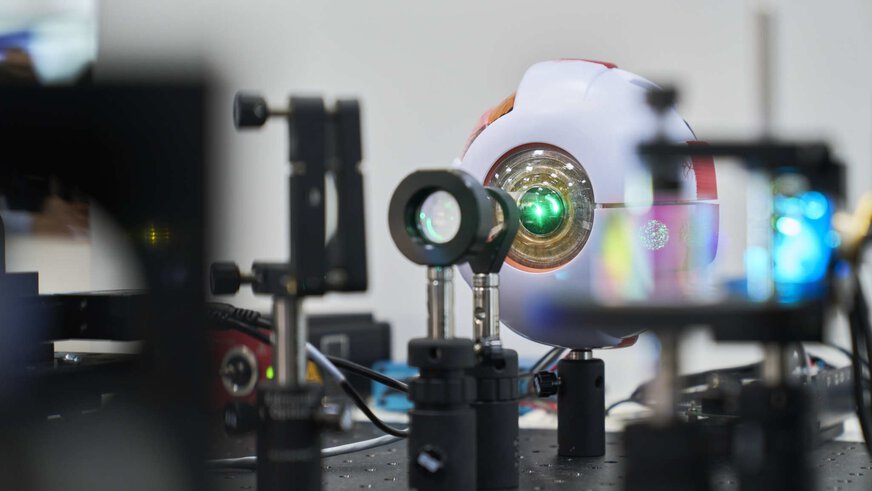 A high-tech optical construction with lenses and an eye-like device on a laboratory table.