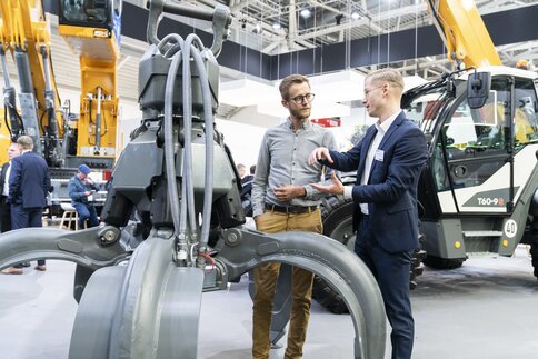 Ein Aussteller spricht mit einem interessierten Besucher neben der ausgestellten Kralle eines Greifbaggers.