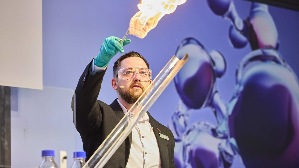 A man in a blazer holds up a metal rod with something burning at the end