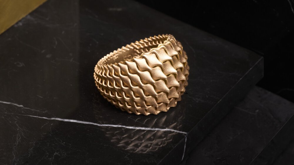 Textured gold bracelet on a black marble surface, with a wavy, intricate design.
