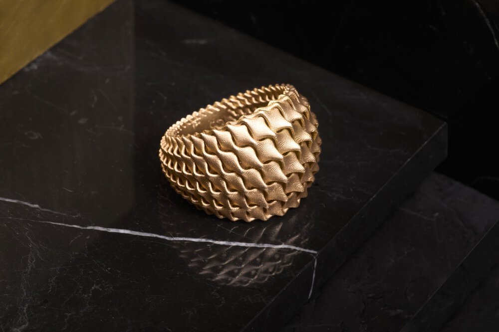 Strukturiertes Goldarmband auf schwarzer Marmoroberfläche, mit gewelltem, kompliziertem Design.