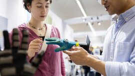 Ein Mann demonstriert einer Frau ein Exponat in Form eines Handschuhs mit einer Platine daran an einem Stand auf der LOPEC.