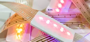 Nahaufnahme von leuchtenden LED-Lichtern die an Bändern von bedruckten Kuststofffolien montiert sind.