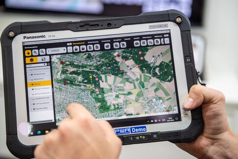 The tablet displays a close-up of a digital forest map with markers