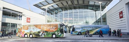 Zwei Busse mit Werbung für Bibione stehen vor einem Messeeingang