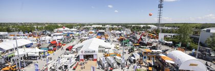 Aerial view of the IFAT open-air grounds with exhibition stands, construction machinery and balloons. The trade fair tower is visible in the background.