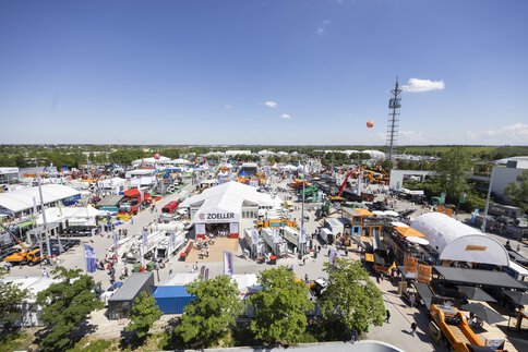 Aerial view of the IFAT open-air grounds with exhibition stands, construction machinery and balloons. The trade fair tower is visible in the background.