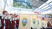 Personen in Tracht mit Blechinstrumenten und der Flagge des Bayerischen Walds treten in einer Messe-Eingangshalle auf.