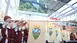 People with brass instruments and the flag of the Bavarian Forest perform in a trade fair entrance hall.