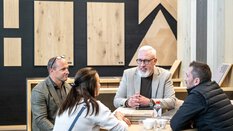 Bei einem Ausstellungsstand auf der BAU sitzen drei Männer und eine Frau an einem runden Tisch und unterhalten sich.