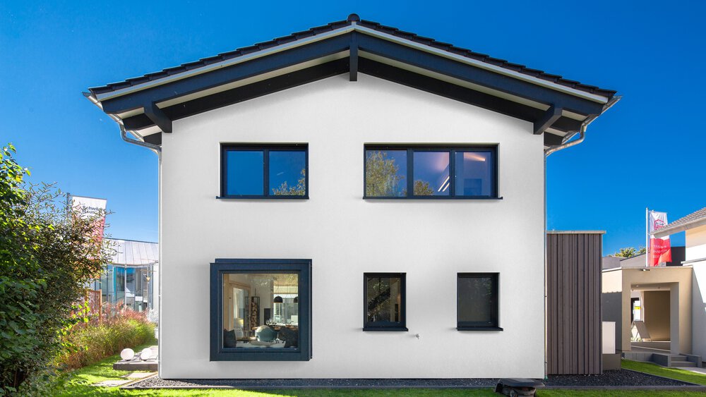 Ein modernes weißes Haus mit Satteldach, großen blauen Fenstern und einem kleinen Garten im Vordergrund.